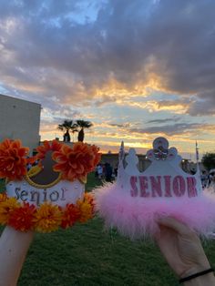 two people holding up crowns with flowers and the word senior on them in front of a cloudy sky