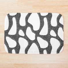 a bath mat with black and white designs on it sitting on a wooden floor next to a wood floor