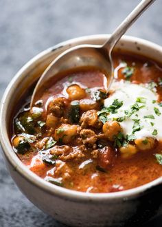 a bowl of soup with meat, beans and sour cream on the spoon in it