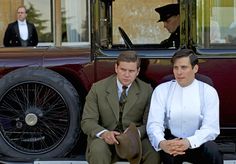 two men sitting next to each other in front of an old fashioned car with another man standing behind them