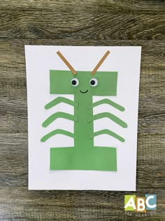 a paper cut out of a green insect with two sticks sticking out of it's back