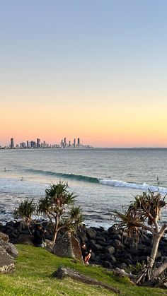 surfers ride the waves in front of an oceanfront cityscape at sunset