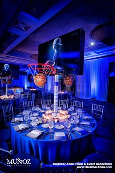 an indoor basketball court is set up for a party with blue lighting and white tablecloths