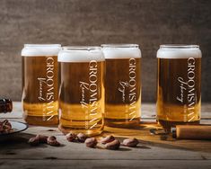 four glasses of beer sitting on top of a table next to nuts and a bottle