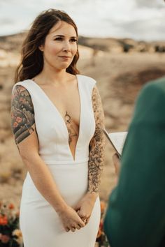 a woman in a white dress standing next to a man with tattoos on his arm