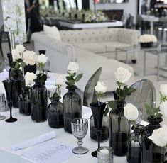 there are many black vases with white flowers in them sitting on the table next to each other