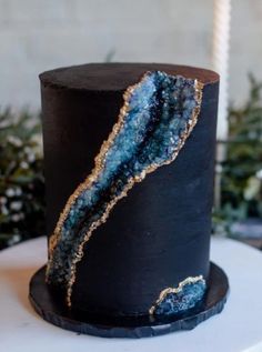 a black cake with gold and blue decorations on it's side, sitting on top of a white table