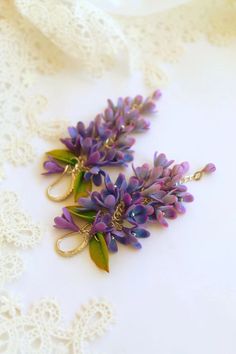 two purple flowers are hanging from gold earwires on a lace tablecloth with white doily