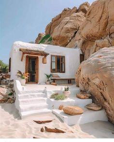 a small white house with steps leading up to the door and windows in between two large rocks