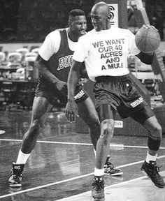 two men playing basketball on an indoor court in black and white photo, one is about to dunk the ball