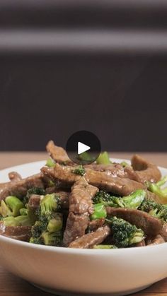 a white bowl filled with meat and broccoli on top of a wooden table