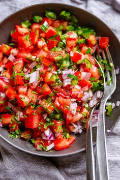 a salad with tomatoes, onions and green peppers in a bowl next to a fork