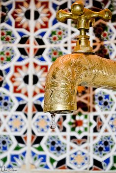 a golden faucet hanging from the side of a wall with colorful tiles behind it