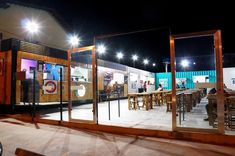 people are standing outside at night in front of an outdoor restaurant with glass doors and tables