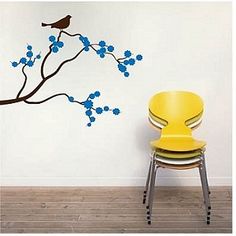 a yellow chair sitting in front of a wall with blue flowers and a bird on it