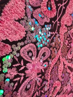 pink and green sequins on black fabric with white flowers in the center,