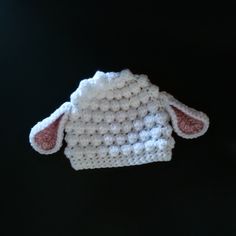 a white crocheted sheep hat hanging from a hook on a black background,