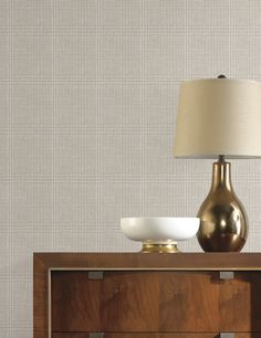 a lamp on top of a wooden dresser next to a white bowl and brown cabinet