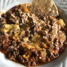 a white plate topped with cheese covered chili and tortilla chips