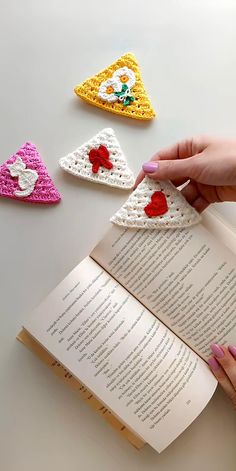 crocheted triangle bookmarks are being held open by a woman's hand