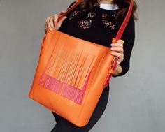 "Original bright leather shoulder hobo bag made of quality natural leather in orange and red color color. Comfortable and durable, it is designed it to be your perfect everyday bag, The red fringe is detachable and the strap has two sides - red and orange. You can wear it two colored and orange only depending on your outfit. The bag features zipper closure, one big inside compartment and leather slip pocket. You won't be unnoticed with this bag! Size: height - 13\"/ 34 cm width - 13\"/ 34 cm dep Orange Leather Hobo Bag For Shopping, Orange Bucket Bag With Adjustable Strap, Orange Bucket Shoulder Bag With Adjustable Strap, Orange Leather Bucket Shoulder Bag, Orange Leather Shoulder Bucket Bag, Orange Leather Bucket Bag For Shopping, Orange Hobo Bag With Removable Pouch For Shopping, Orange Leather Hobo Bag For Daily Use, Orange Bucket Bag With Removable Pouch For Shopping