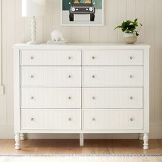 a white dresser sitting in a living room next to a lamp