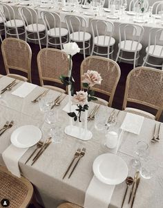 a table set with white plates and silverware, flowers in vases on the tables