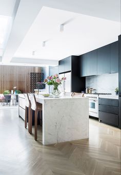 a kitchen with black cabinets and white marble counter tops, along with wooden flooring