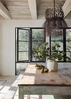 a table with some fruit on it in front of two windows and a chandelier