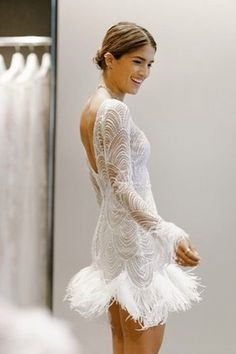 a woman in a short white dress standing next to a mirror