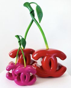 two red and pink vases with green stems sticking out of them on a white surface