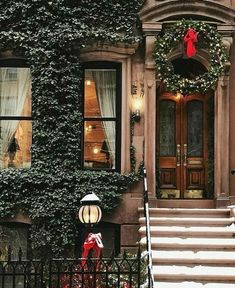 a house covered in ivy and christmas wreaths with stairs leading up to the front door