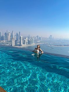 a woman sitting in the middle of a swimming pool next to a cityscape