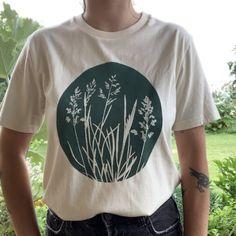 a man wearing a t - shirt that has plants on it and is standing in front of some bushes