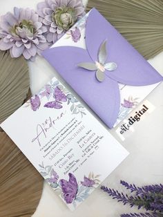 a purple and white wedding card with flowers on it, next to some other items