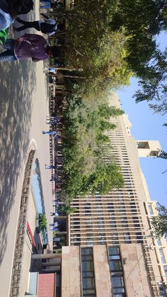 people are walking down the street in front of tall buildings with trees on both sides