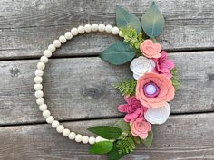 a wreath made out of felt flowers on a wooden surface with greenery and beads