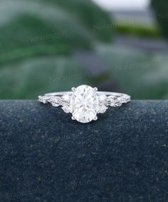 a close up view of a diamond engagement ring on a blue surface with greenery in the background