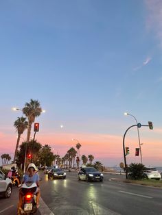 a man riding a motorcycle down a street next to tall palm trees and traffic lights