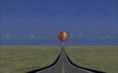 an image of a balloon flying in the sky over a road that is lined with grass