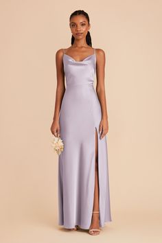 a woman wearing a lavender colored dress with a slit down the side, and holding a flower in her hand