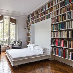 there is a bed in the room with many books on the wall and shelves full of books