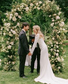 a bride and groom holding hands in front of a floral arch