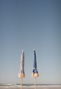 two beach umbrellas sitting on top of a sandy beach