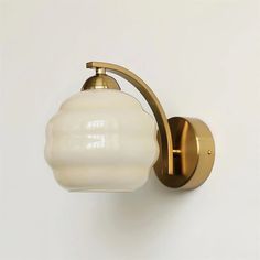 a wall light with a white glass shade on it's arm and an antique brass finish