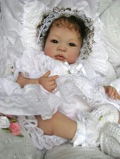 a baby doll wearing a white dress and holding a teddy bear in it's lap