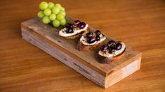 small appetizers are arranged on a wooden board with grapes and bread in the middle