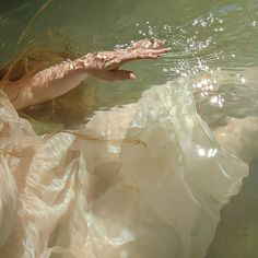 a woman is floating in the water wearing a white dress and holding her hand out