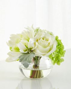 a vase filled with white and green flowers on top of a glass table next to a window