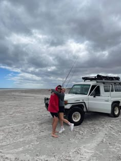 two people standing in front of a truck with a fishing pole on it's roof